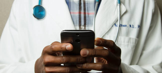 Person im Arztkittel mit Stetoskop und einem Smartphone in der Hand